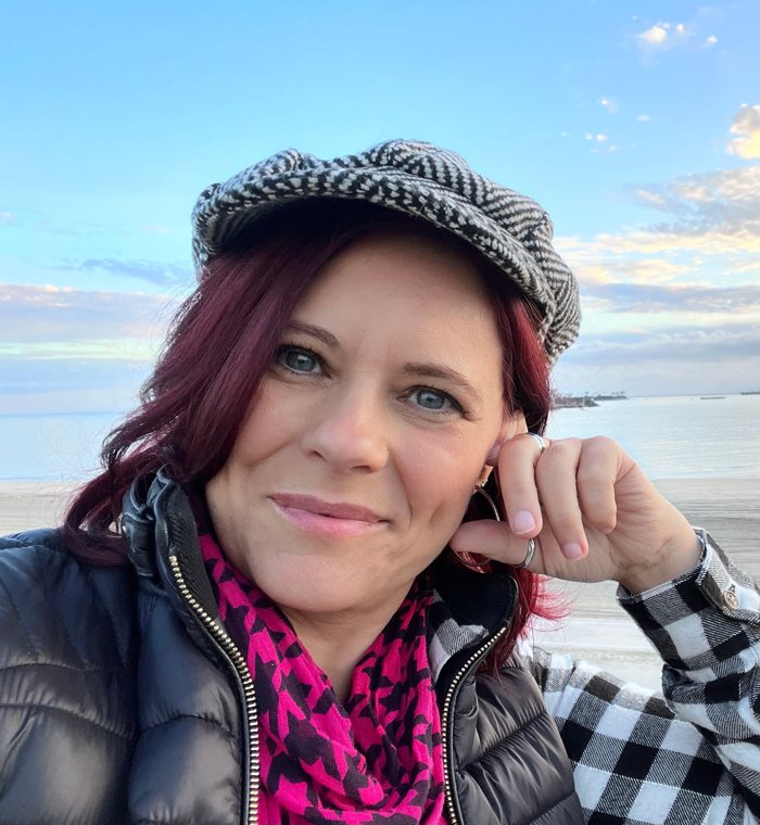 Sabrina Brimhall at the beach in a herringbone cap and magenta scarf